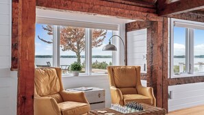 Ein gemütliches Zimmer mit zwei Ledersesseln, einem Korbtisch und Blick auf einen See durch große Fenster.