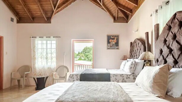 A bedroom with two beds, a wooden ceiling, a window with a view, and a painting on the wall.