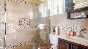 A bathroom with a glass shower enclosure, a toilet with a brown seat cover, and a sink with a mirror above it.