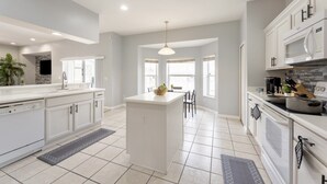 A modern kitchen with white cabinetry, a central island, and a dining area with natural light. - Modern 5BR Family Home w/ Private Pool Near Disney (Davenport)