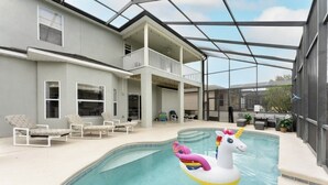 A swimming pool with a unicorn float, lounge chairs, and a covered patio area. - Modern 5BR Family Home w/ Private Pool Near Disney (Davenport)