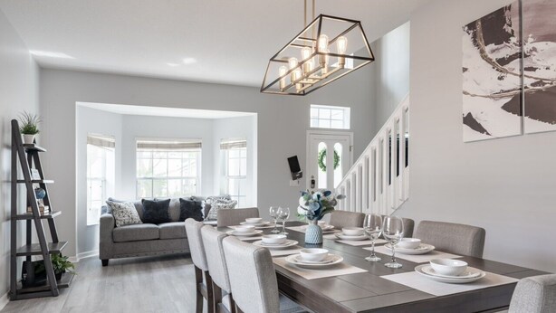 A dining area with a long table set for six, a staircase, and a view of a living room with a sofa and a ladder. - Modern 5BR Family Home w/ Private Pool Near Disney (Davenport)