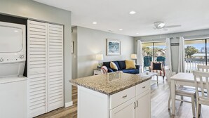 A modern kitchen with a granite countertop, white cabinets, and a dining area with a table and chairs. - Sandpiper Cove 3202 2 Bedroom Condo by RedAwning (Destin)