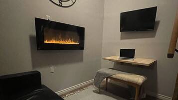 Un salon chaleureux avec une cheminée, un téléviseur fixé au mur, un ordinateur portable posé sur une table en bois et un élément de décoration murale en forme d’étoile.