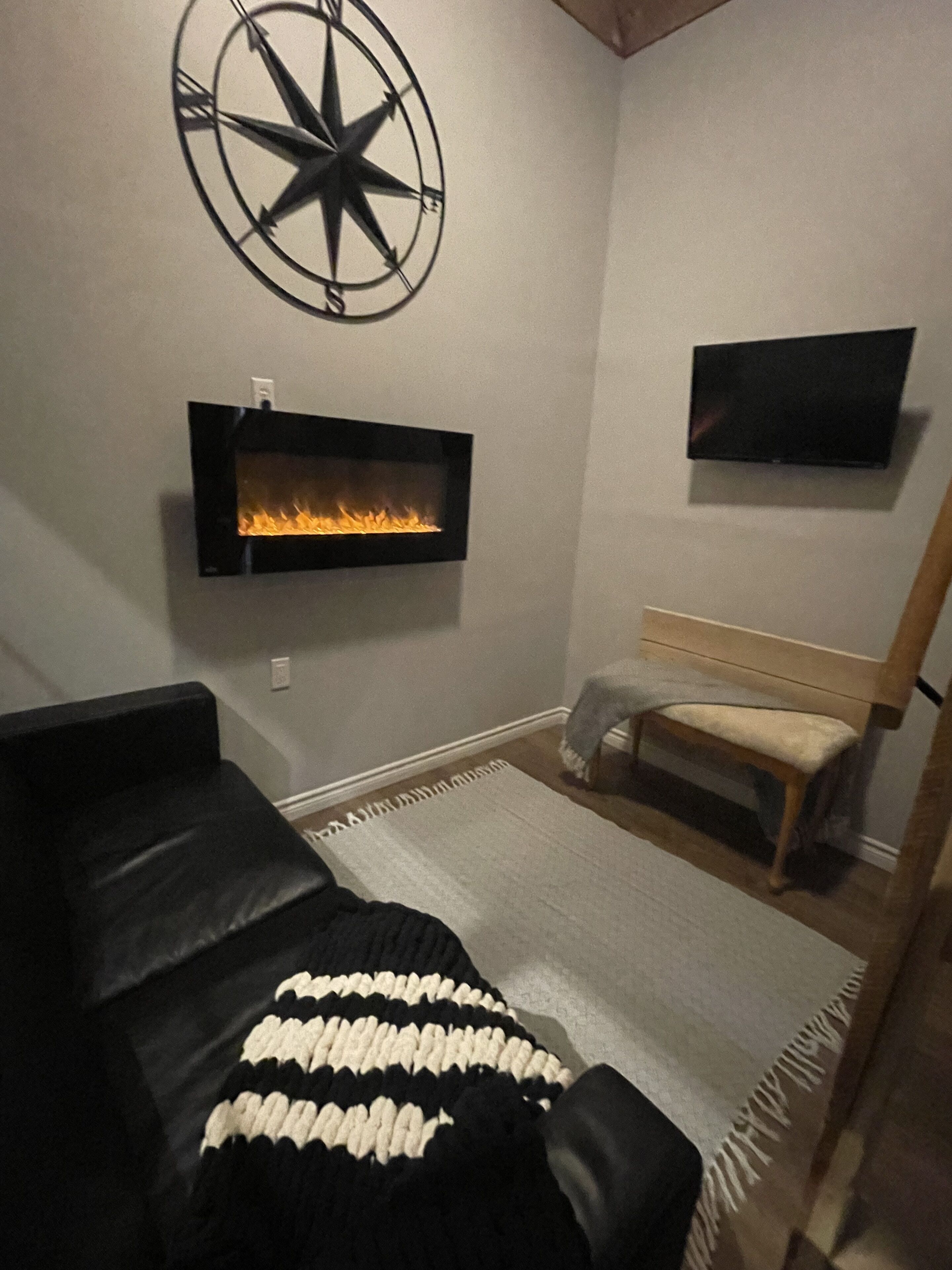 Un salon moderne doté d’une cheminée, d’un téléviseur fixé au mur, d’une grande horloge murale et d’un coin salon confortable.