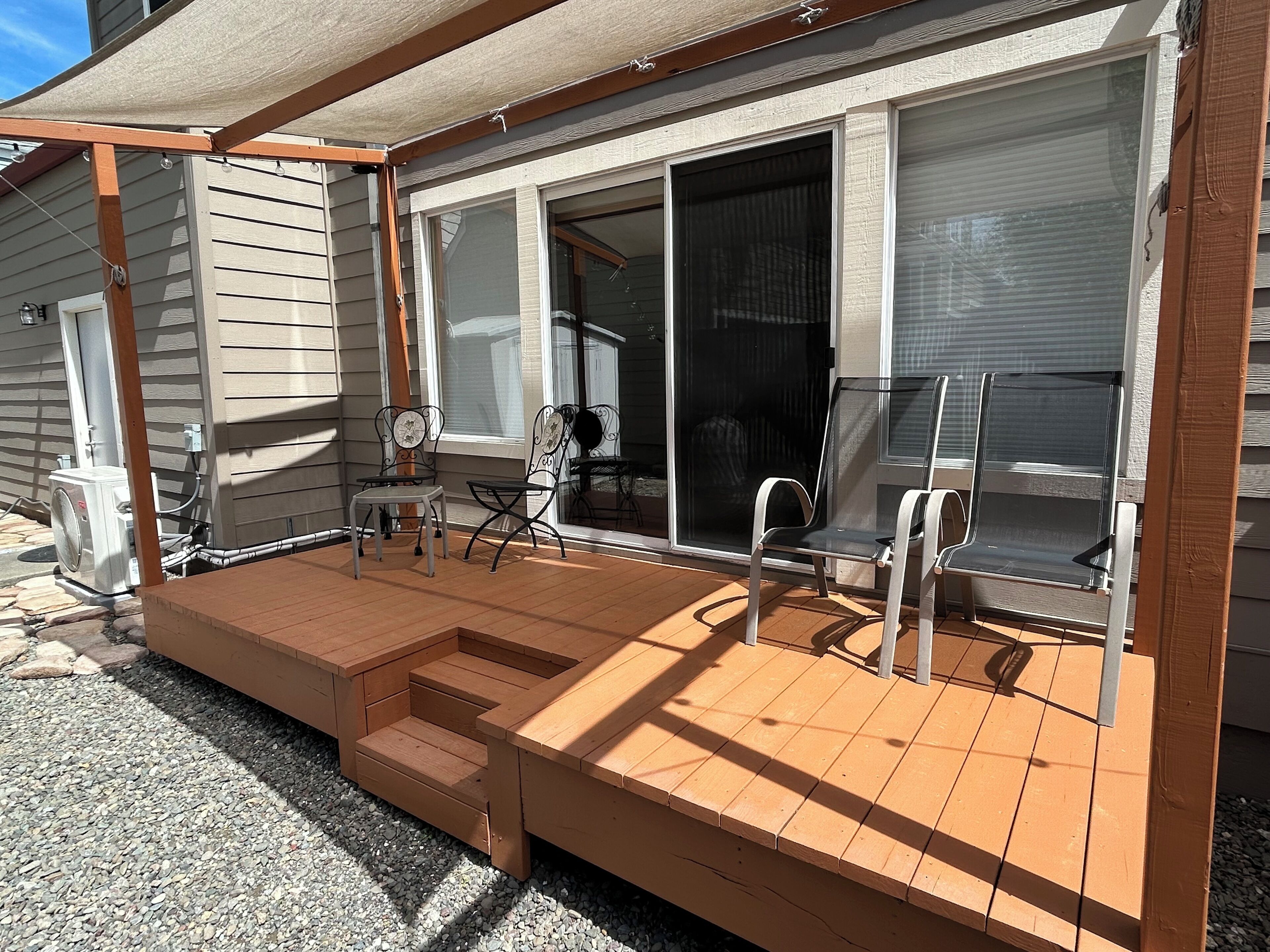 A covered patio with a wooden deck, outdoor seating, and a sliding glass door leading to a screened-in area.