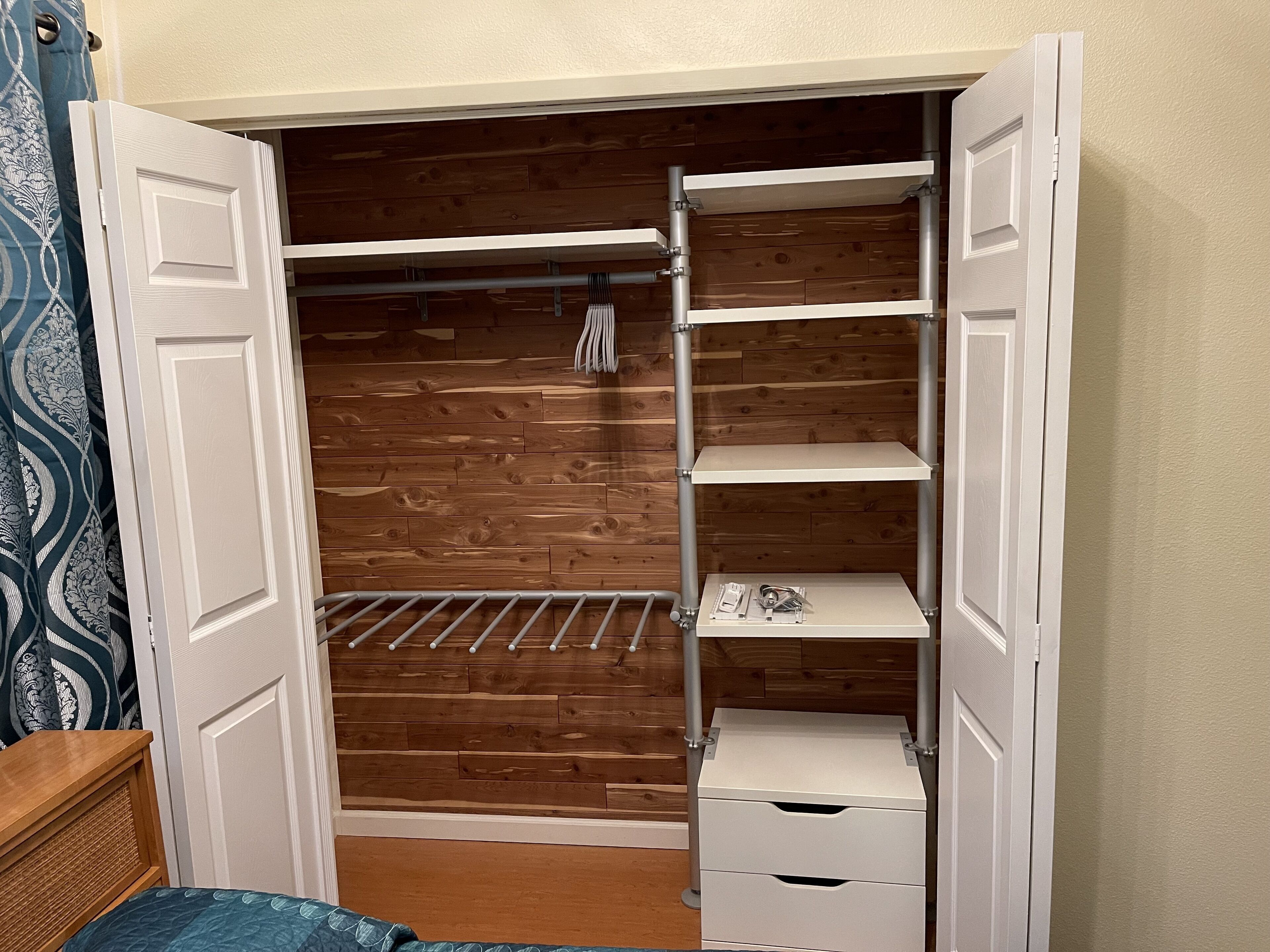 A walk-in closet with wooden paneling, metal shelving, and a bed with a blue quilt.