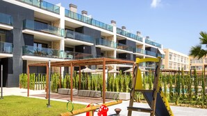 A playground with seesaws and a slide, surrounded by a well-maintained lawn and a building with balconies. - Golden Ray Sun by Interhome (Jávea)