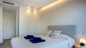 A modern bedroom with a large bed, a bedside table with a lamp, and a wardrobe. - Golden Ray Sun by Interhome (Jávea)
