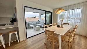 A modern kitchen with a dining area, a sofa, and a view through a glass door. - Coffs Harbour Beach House (Coffs Harbour)