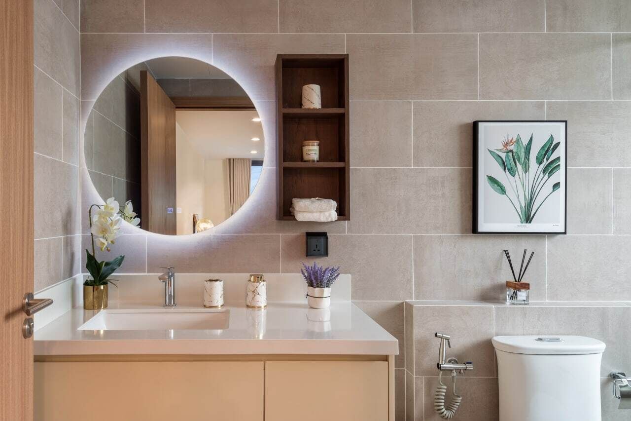 A modern bathroom with a round mirror, a sink, a toilet, and a shelf with toiletries.
