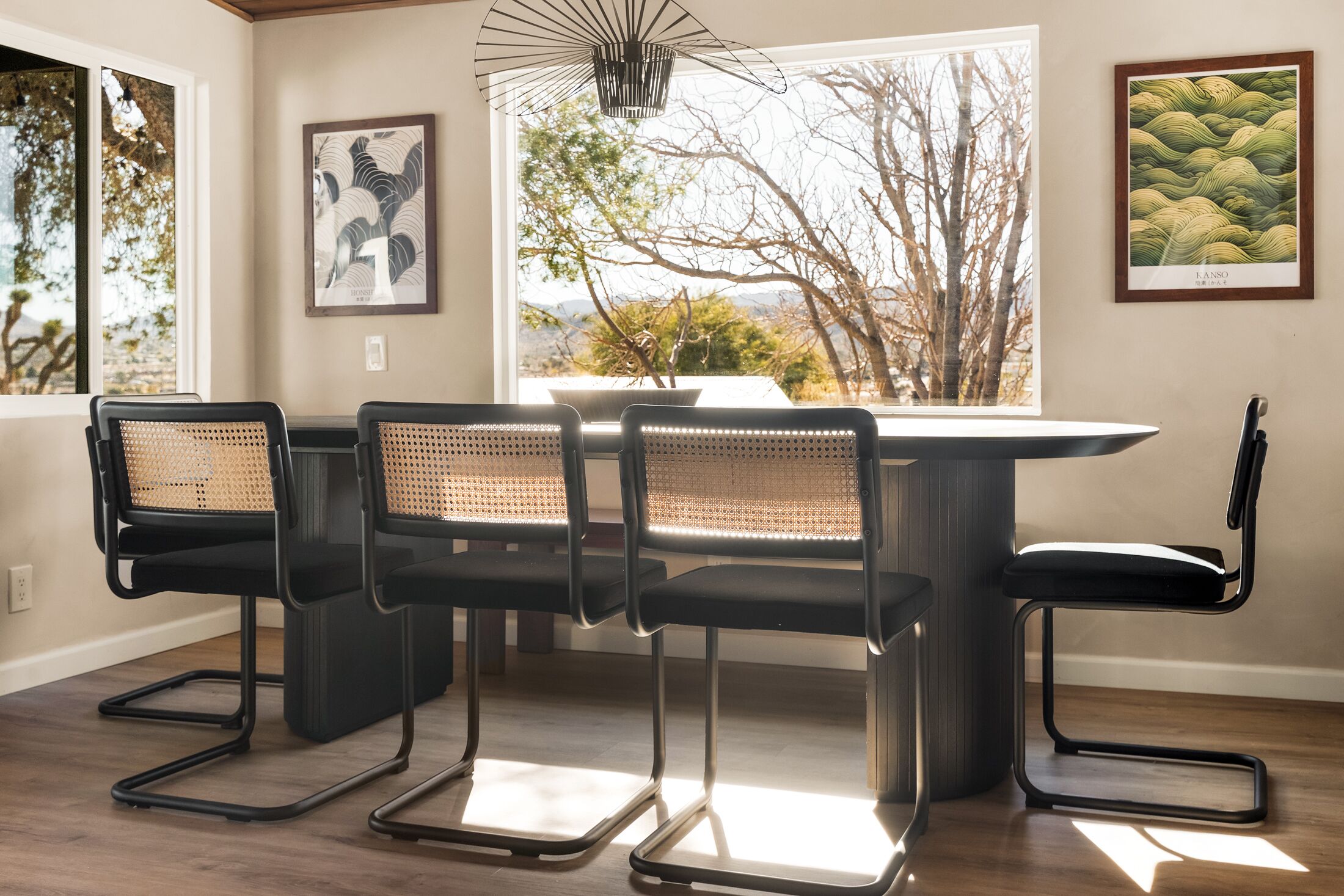 A dining area with a round table and four chairs, a pendant light, and artwork on the walls.