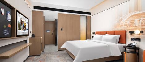 Habitación de hotel moderna con una cama grande, un escritorio y un televisor. Se observa un armario de madera y una pequeña mesa con una lámpara.