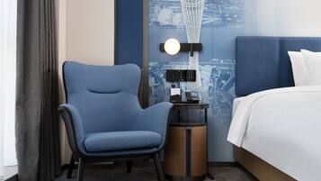 A hotel room with a blue chair, a bedside table with a lamp, and a bed with white linens.