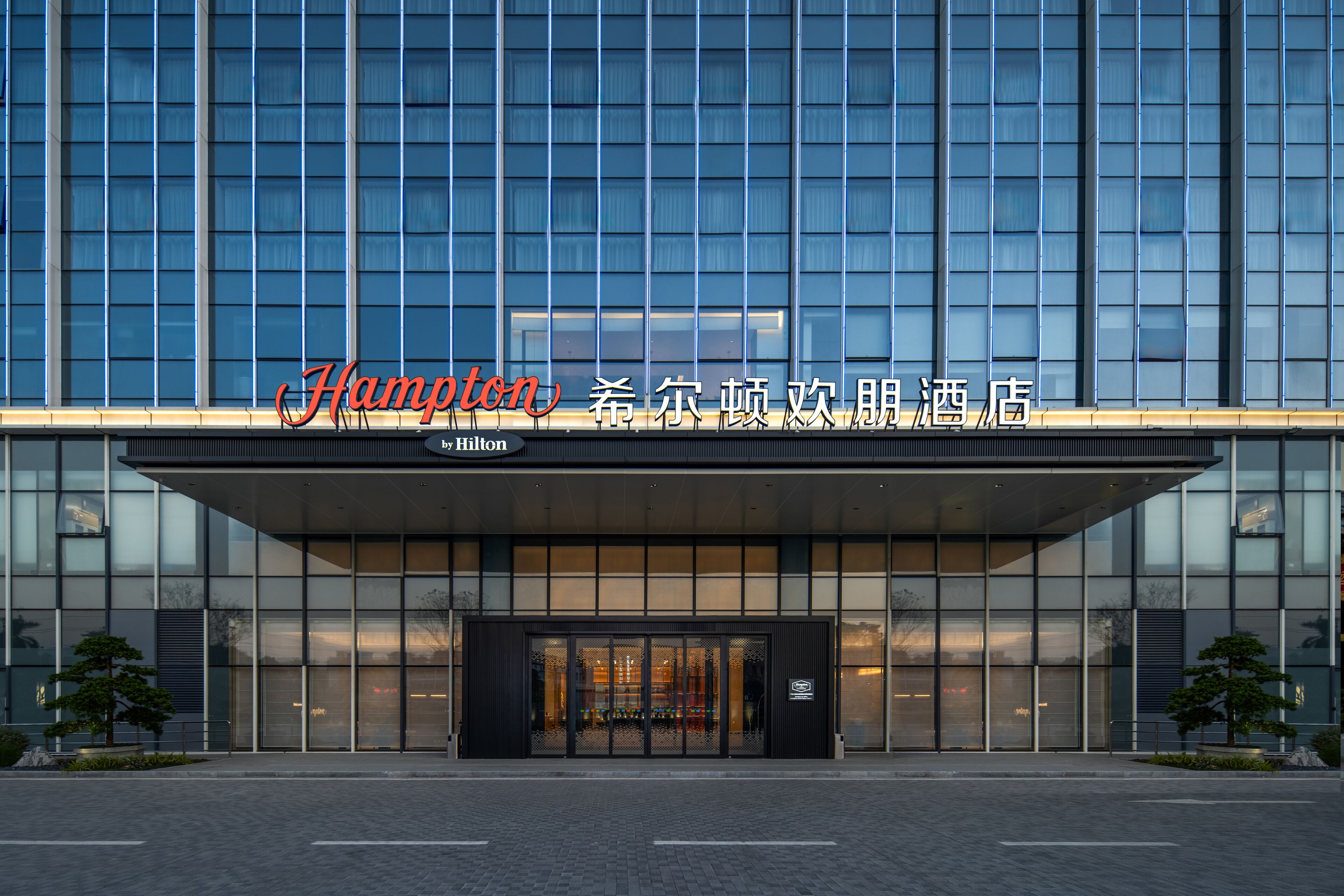 A modern hotel with a glass facade, a prominent entrance, and a sign reading "Hampton."
