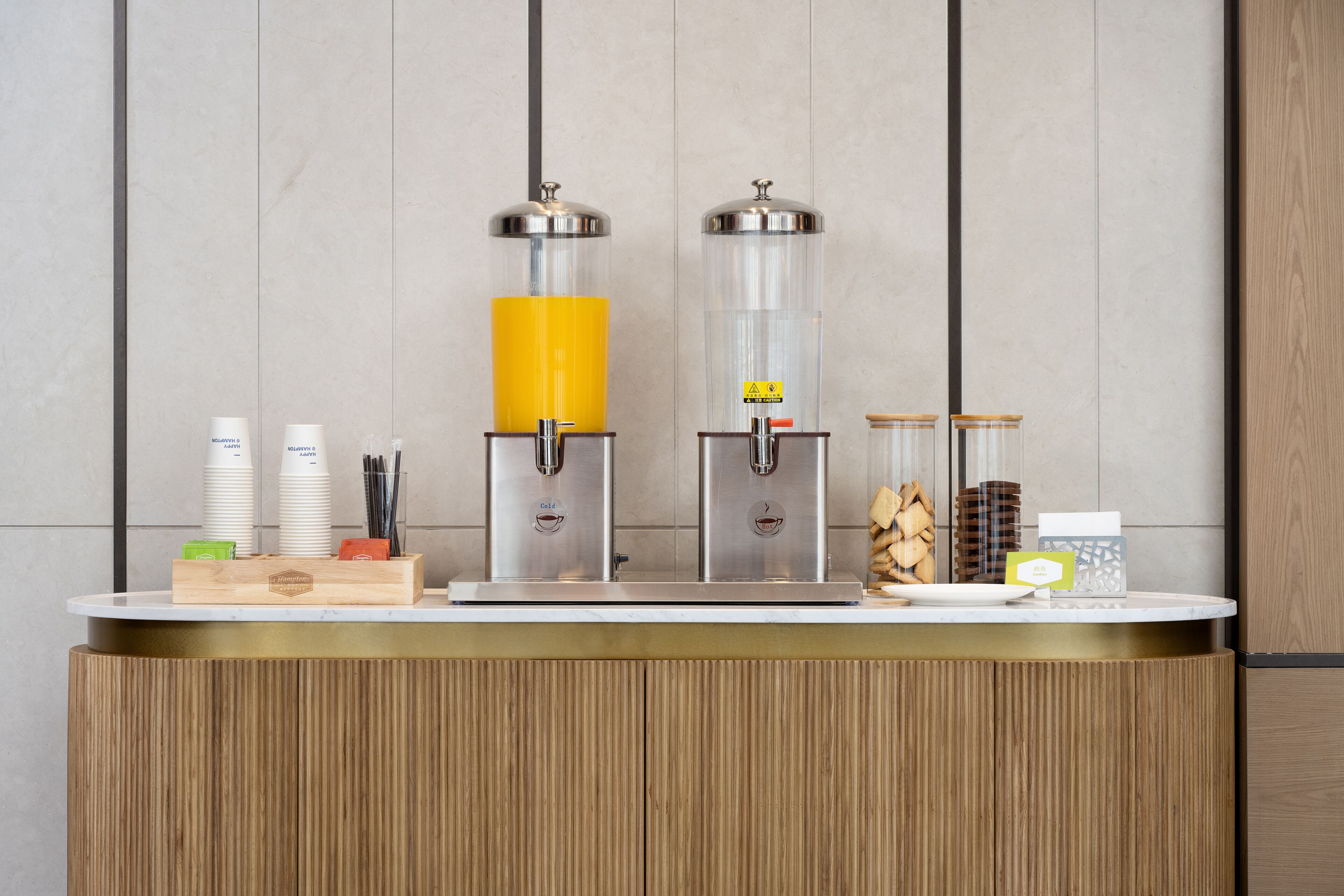 A modern coffee station with two dispensers, a wooden counter, and various coffee-related items.
