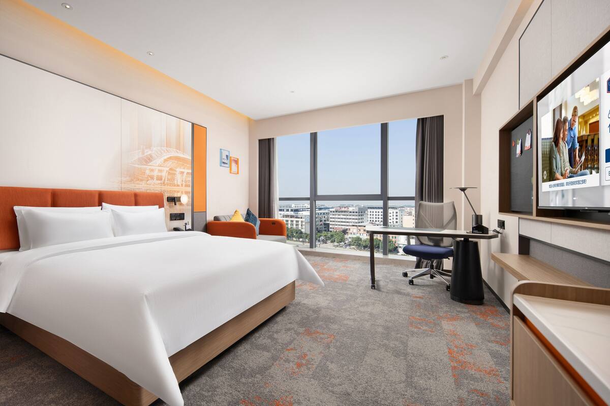 Una habitación de hotel moderna con una cama grande, un escritorio, una silla y un televisor.