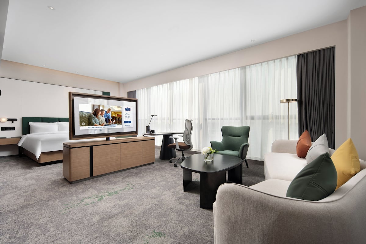 Habitación de hotel con cama, escritorio, televisor, sofá y mesa de centro.