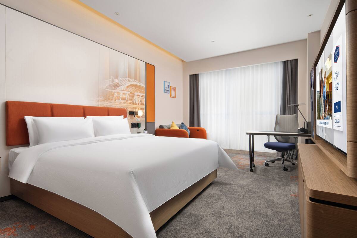 Una habitación de hotel moderna con una cama grande, un escritorio y un televisor.