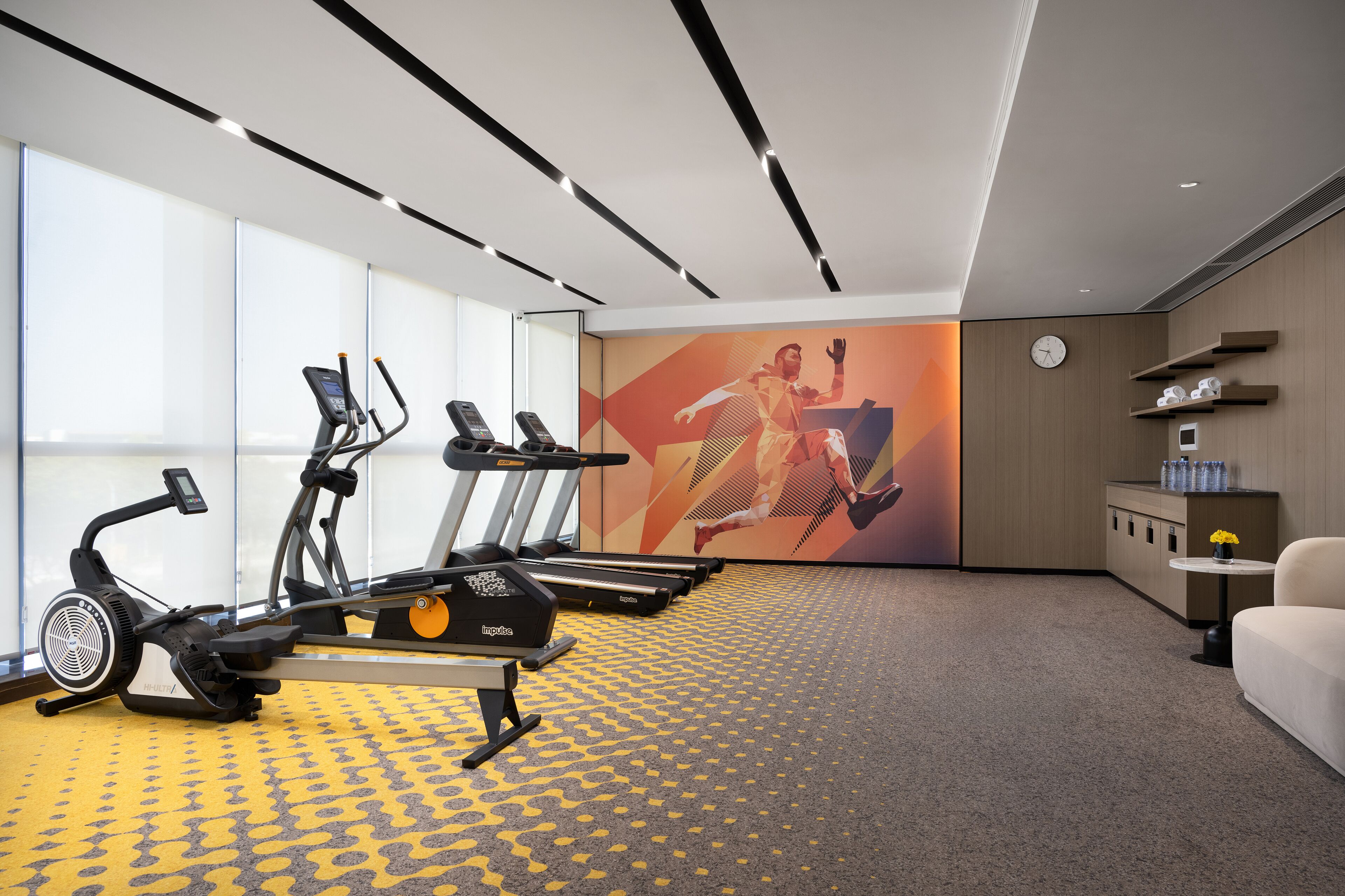 Une salle de sport moderne équipée de vélos d’appartement, de tapis de course et d’une grande fresque murale destinée à motiver les utilisateurs.