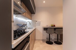 A modern kitchen with a gas stove, sink, and bar stools. - North Medellin Luxury Cozy and Classy Apartment near Downtown (Medellín)