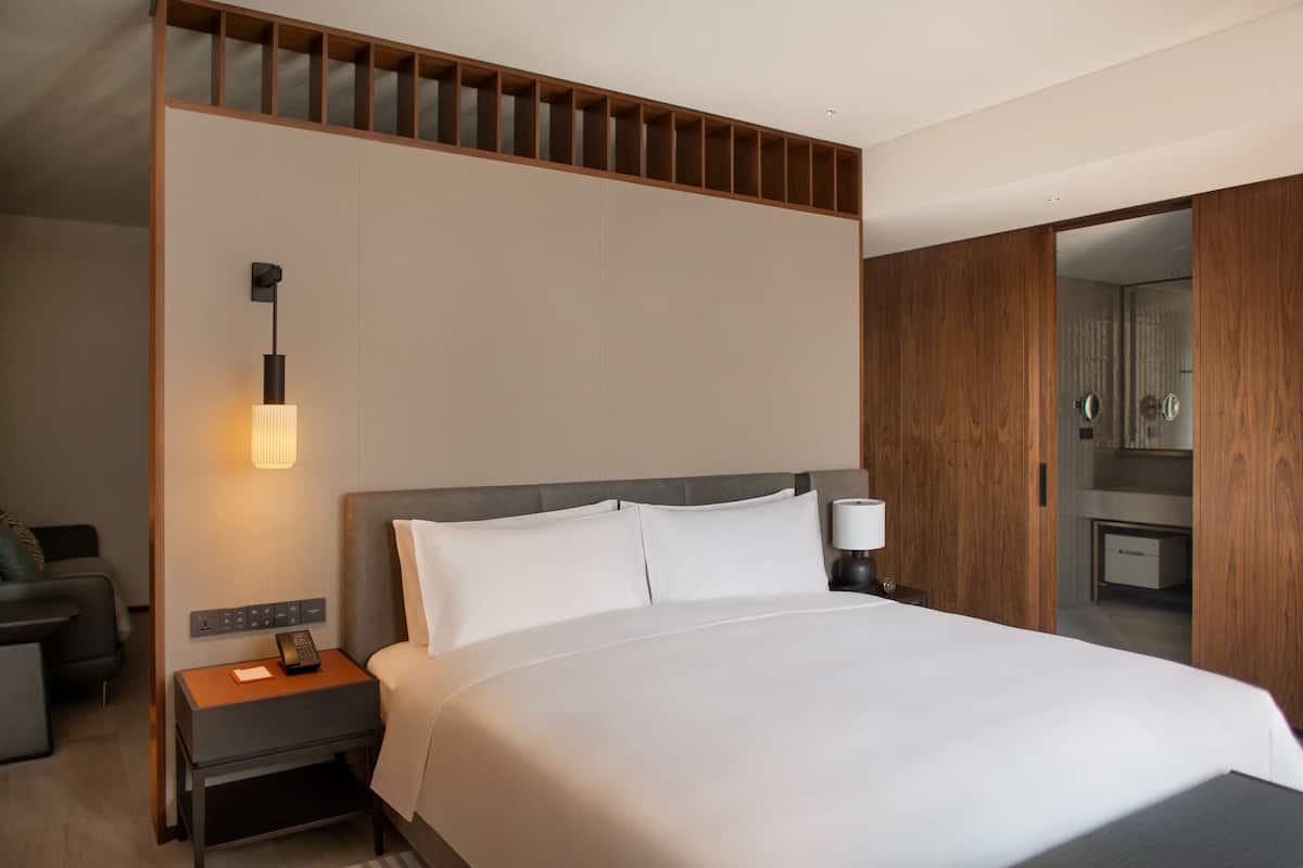 Een moderne hotelkamer met een groot bed, een nachtkastje met een lamp, een telefoon op een nachtkastje en een houten garderobe.