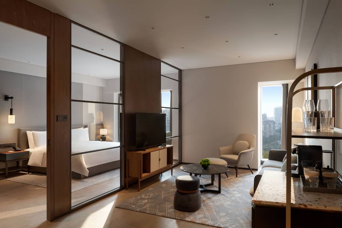 Een moderne hotelkamer met een groot bed, een televisie, een zithoek met een tafel en stoelen, en uitzicht op de stad.