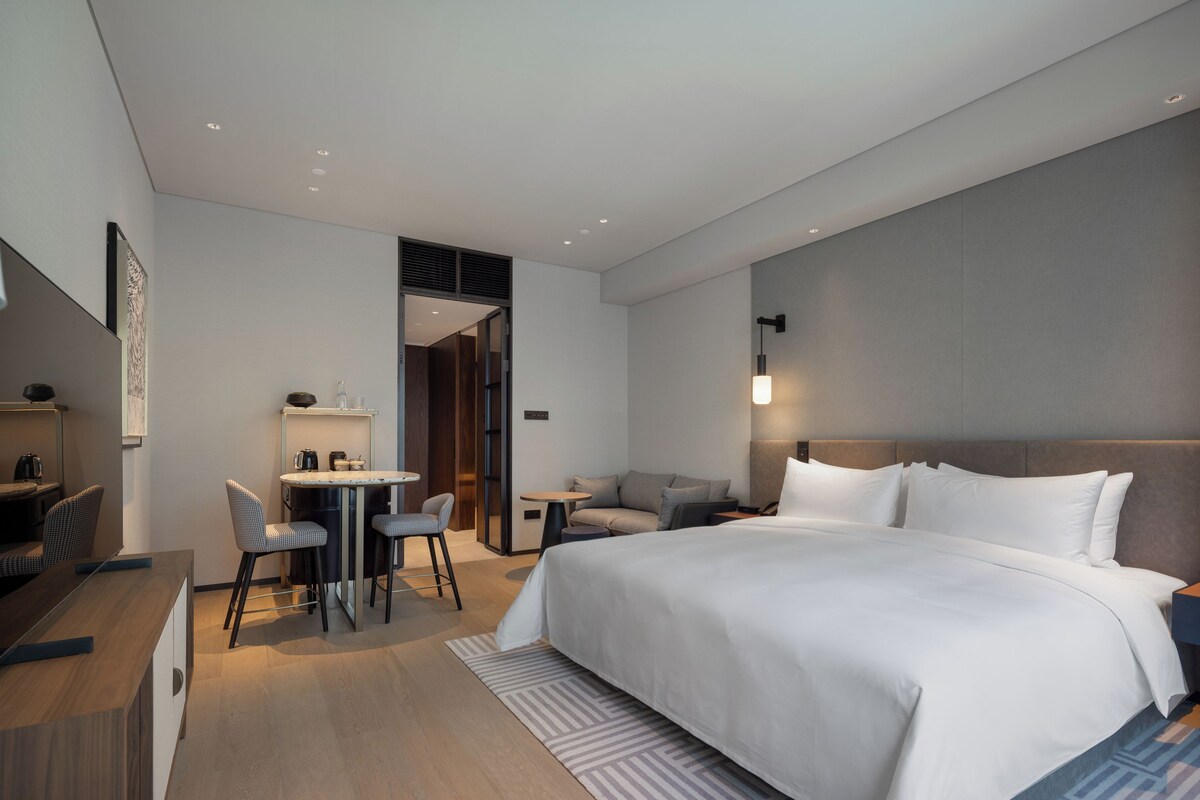 Una habitación de hotel moderna con una cama grande, un escritorio con sillas, una mesita pequeña y un sofá.