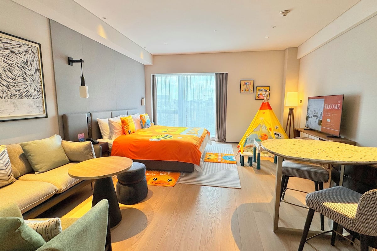 Hotelkamer met een bed, een slaapbank, een eettafel, stoelen, een kleine speeltent en een televisie.