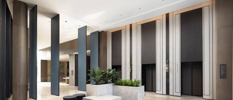 A modern lobby with a herringbone floor, large columns, and a central seating area with planters.