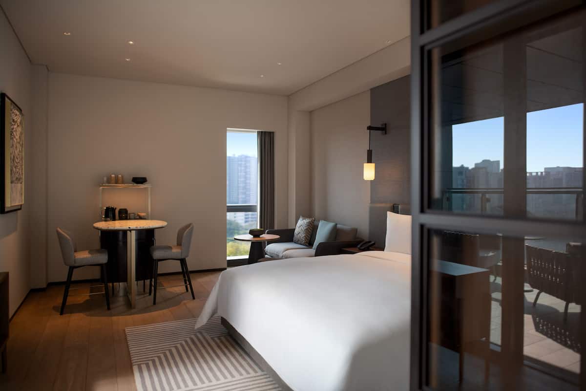 Een moderne hotelkamer met een groot bed, een zithoek met stoelen, een kleine tafel met een koffiezetapparaat en uitzicht op de stad.