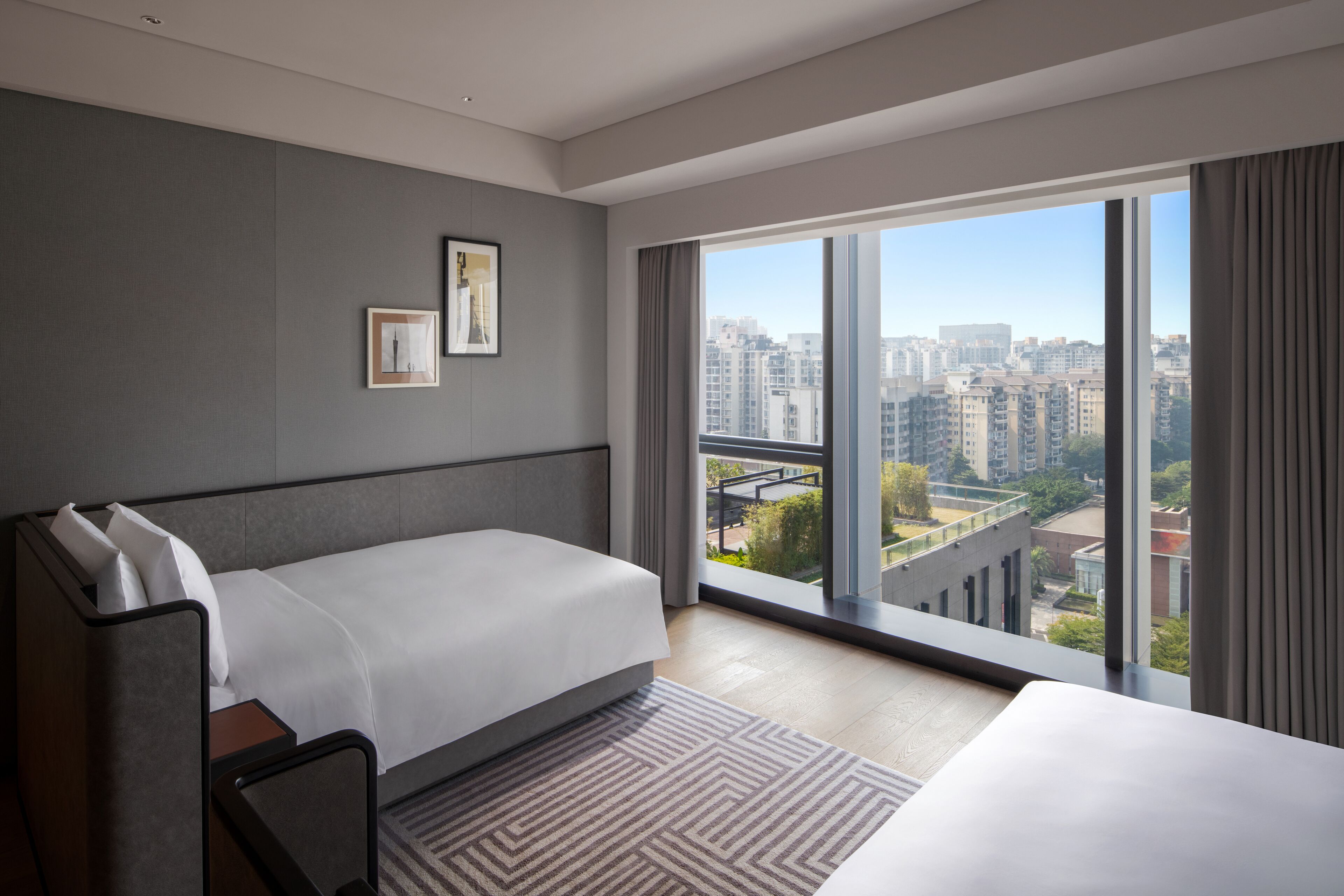 Habitación de hotel moderna con una cama grande, un escritorio pequeño y vistas de la ciudad a través de amplios ventanales.