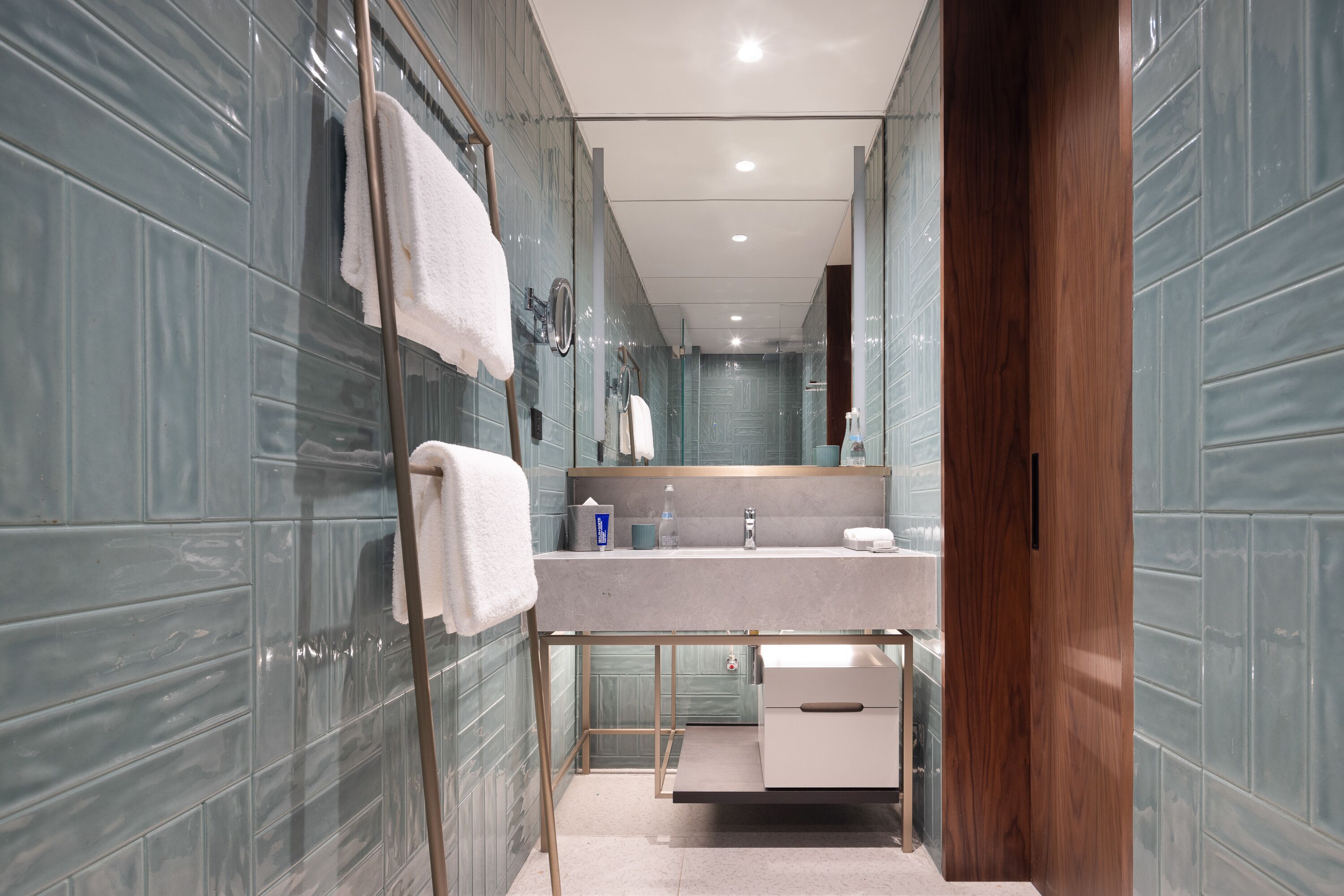 A modern bathroom with a glass shower enclosure, a vanity with a mirror, and a wooden door.
