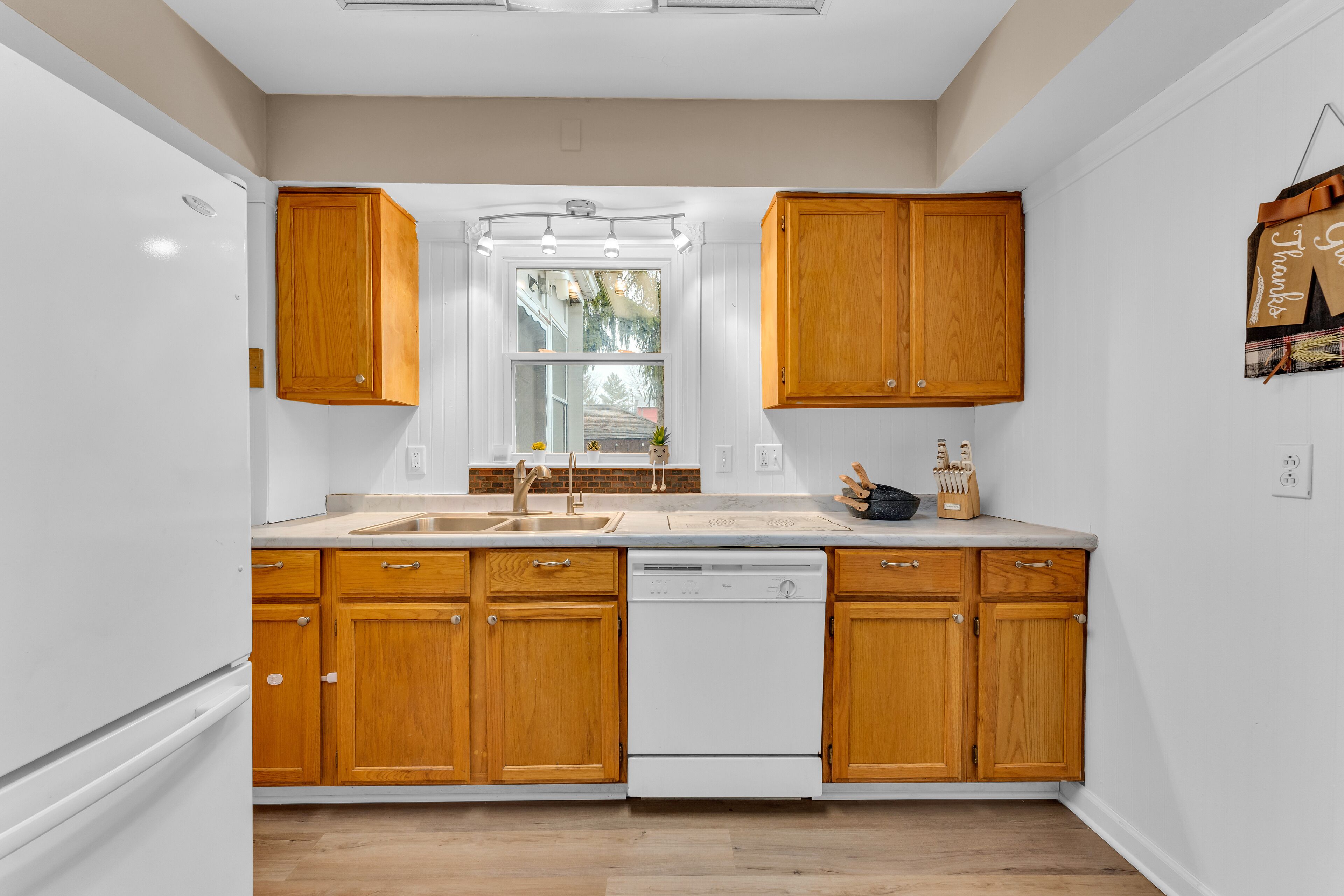 A kitchen with wooden cabinets, a white dishwasher, and a window above the sink.
