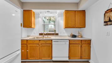 A kitchen with wooden cabinets, a white dishwasher, and a window above the sink.