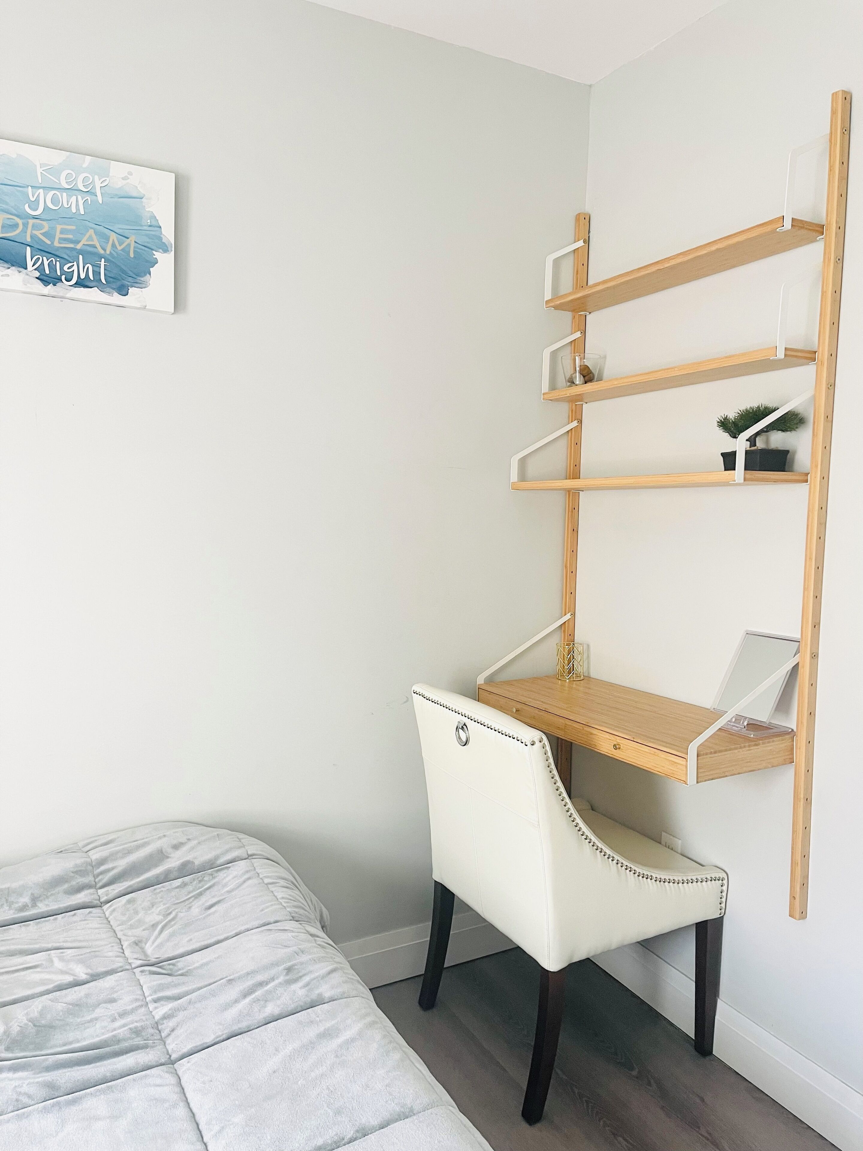 Quarto com cama, escrivaninha com prateleiras e um cartaz motivacional.