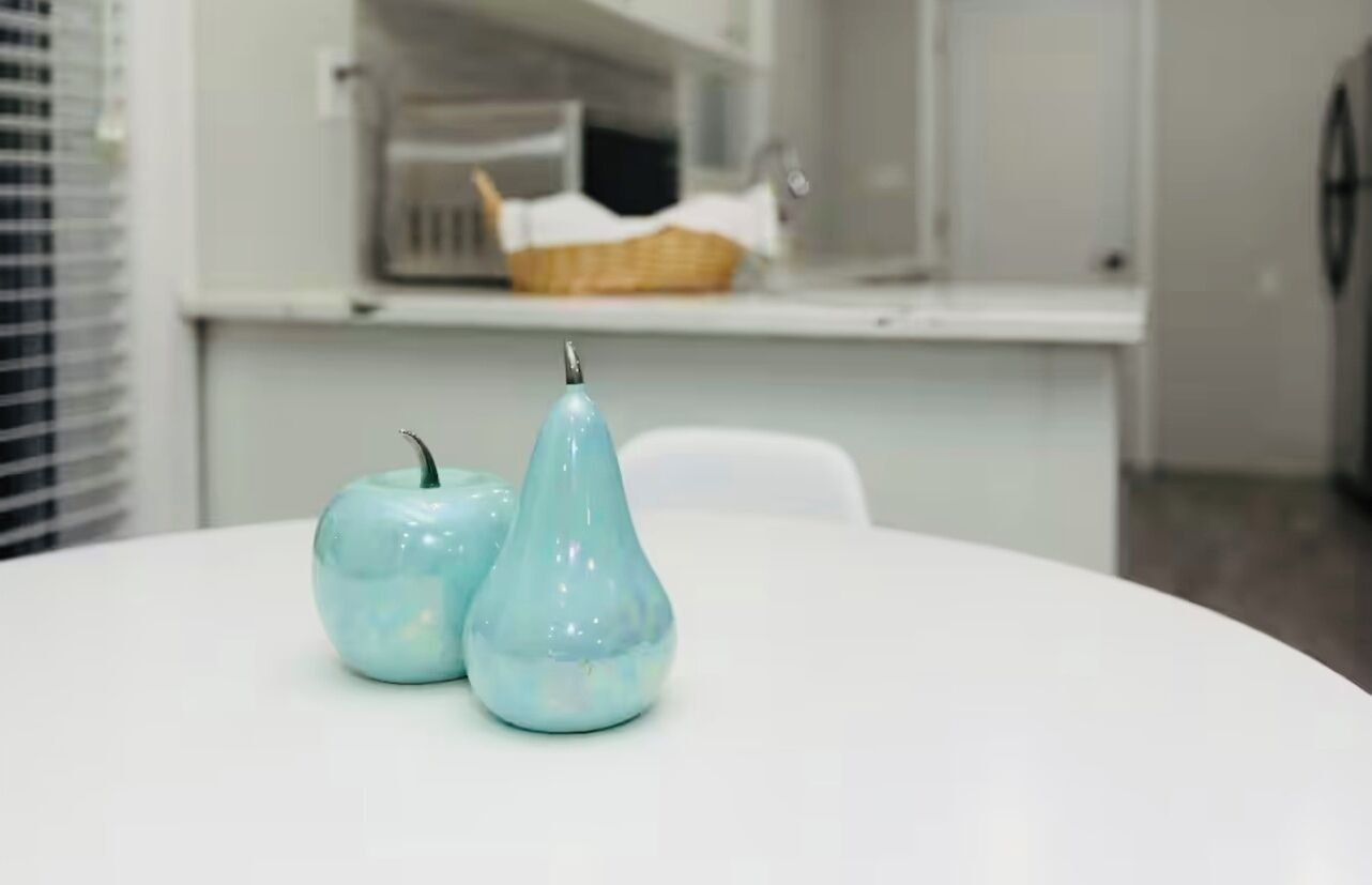 A white table with two ceramic vases, one apple-shaped and one pear-shaped, on a modern kitchen counter.