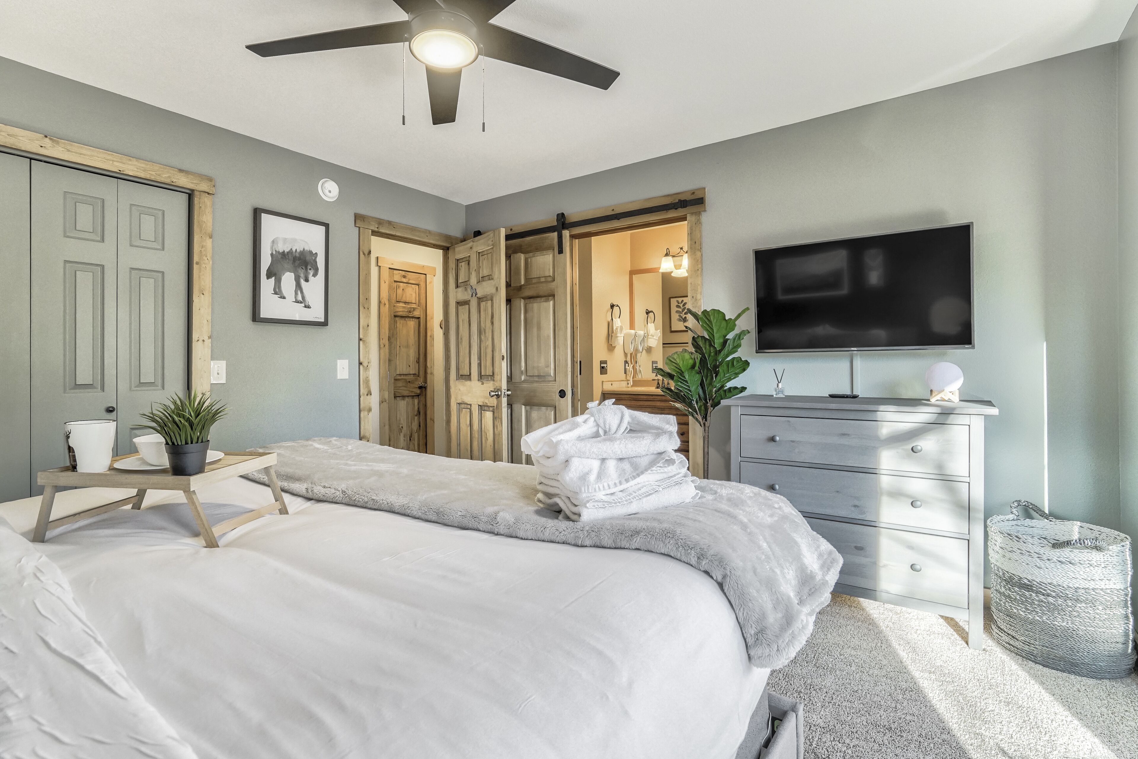 A bedroom with a bed, a dresser, a television, and a door leading to another room.