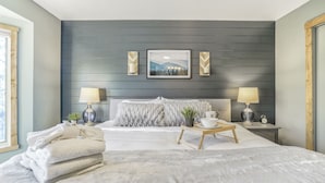 Una camera da letto moderna con un letto grande, due comodini con lampade, un quadro appeso al muro e una finestra sul lato sinistro.
