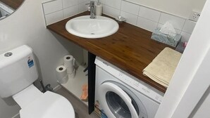 A compact bathroom with a sink, toilet, and washing machine. - Ohope Dreamer 1 (Ōhope)