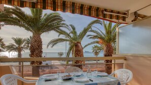 Un balcón con una mesa lista para comer, con vista a una playa con palmeras y el mar.