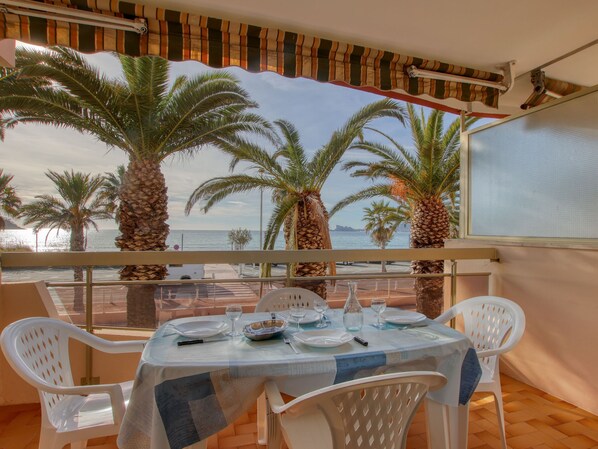 A balcony with a table set for dining, overlooking a beach with palm trees and the sea. - Dio Brasil by Interhome (Saint Cyr sur mer Les Lecques)