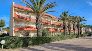 Un hotel de varios pisos con balcones, palmeras y un estacionamiento.