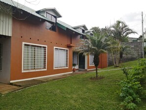 A two-story house with a flat roof, large windows, and a small garden with a palm tree.