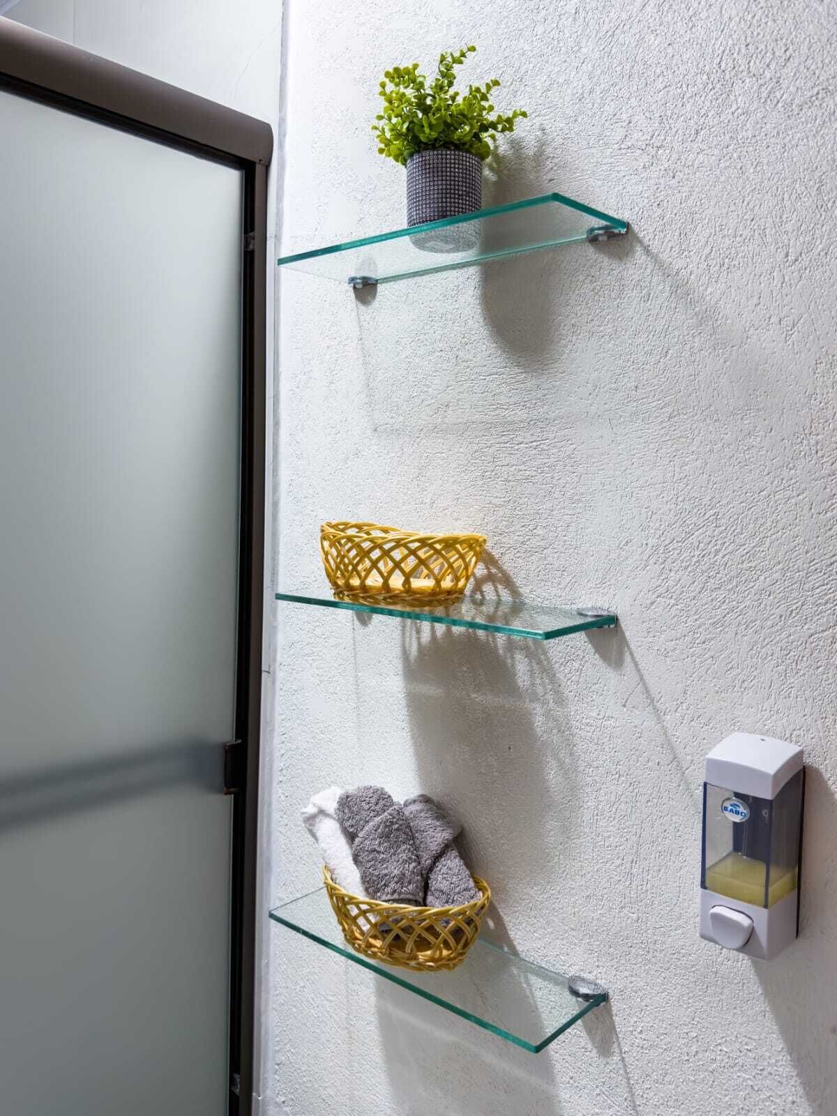 A wall-mounted shelf unit with three glass shelves, each holding a decorative basket and a potted plant.