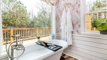 Un baño con una bañera independiente, terraza de madera en el exterior y vistas a árboles.
