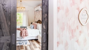 A bedroom with a bed, a chandelier, and a window with curtains.