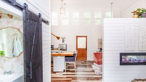 A room with a wooden floor, a desk with a chair, a red chair, a fireplace, and a sliding door.