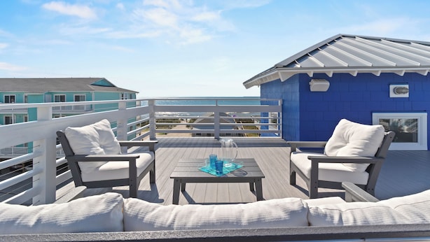 Una terrazza con due poltrone bianche imbottite e un tavolino, con vista sulla spiaggia e un edificio blu.