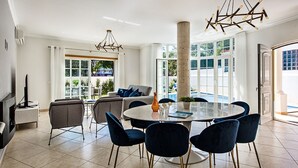 Een moderne eetruimte met een ronde tafel, blauwe stoelen en een bijzondere kroonluchter.